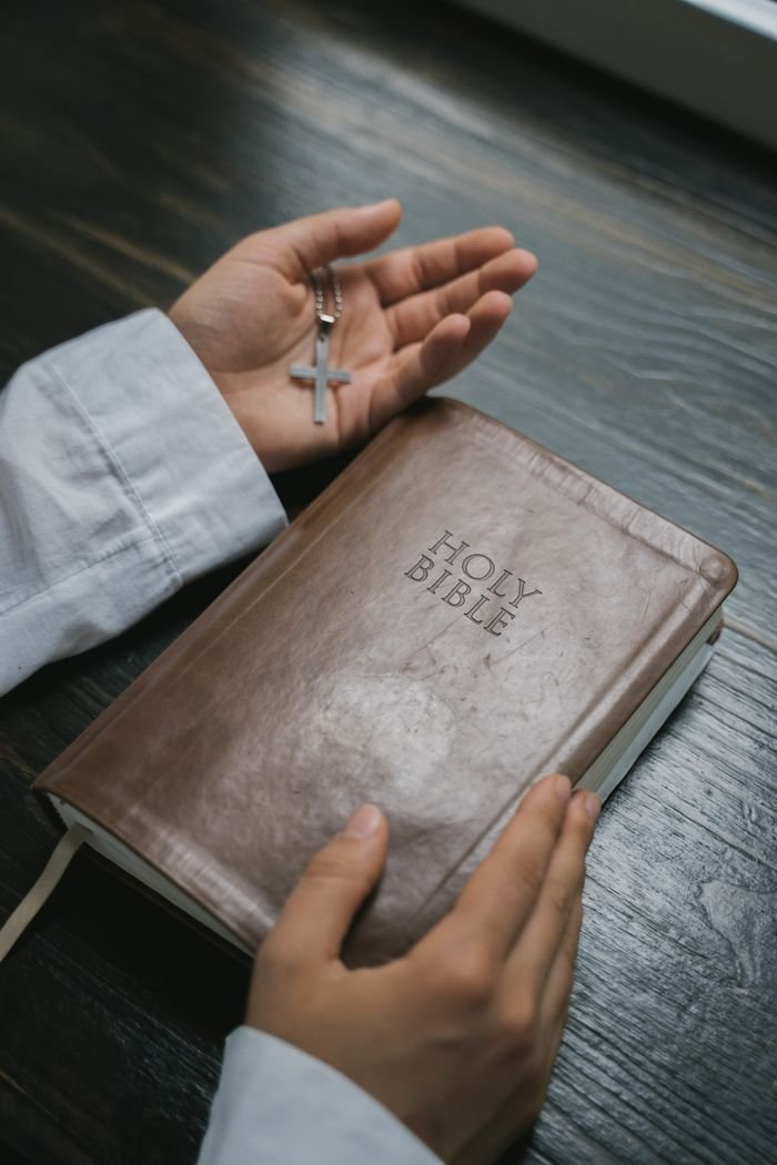 services-02 Close-up of hands holding a Holy Bible with a cross necklace, symbolizing faith and spirituality.